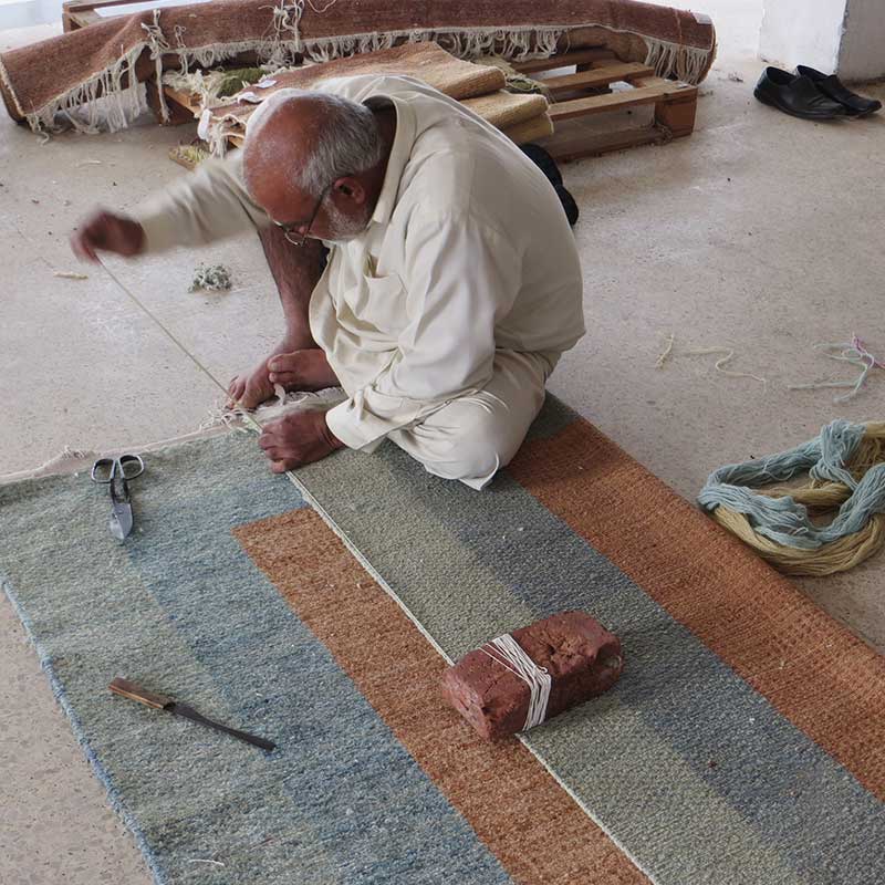 手織りの絨毯を織っている職人さん